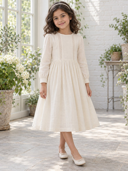 Robe de demoiselle d'honneur simple et pudique, longueur thé, couleur crème, avec empiècements en dentelle fine, manches longues, larges poignets, coupe trapèze froncée et boutonnage au dos